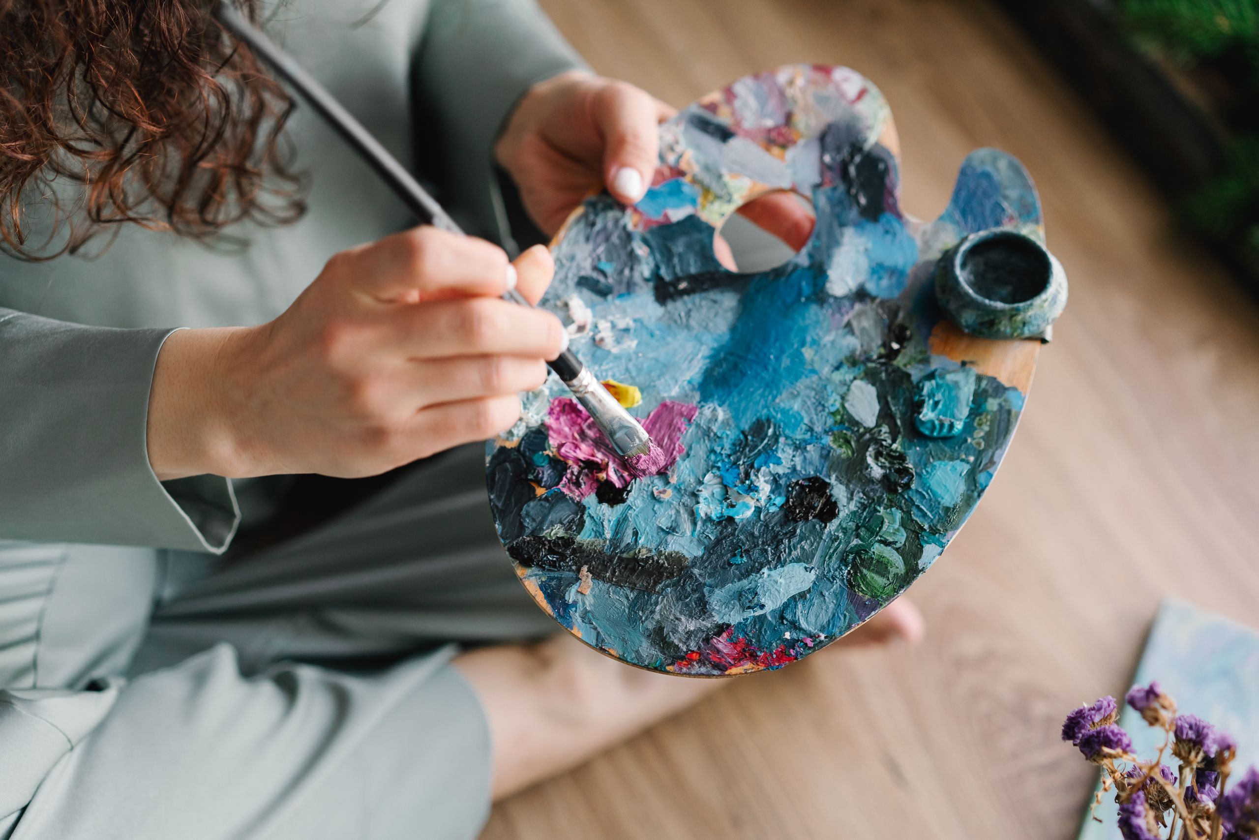 Close-up of hands painting on a colorful palette, showcasing creativity and artistry.