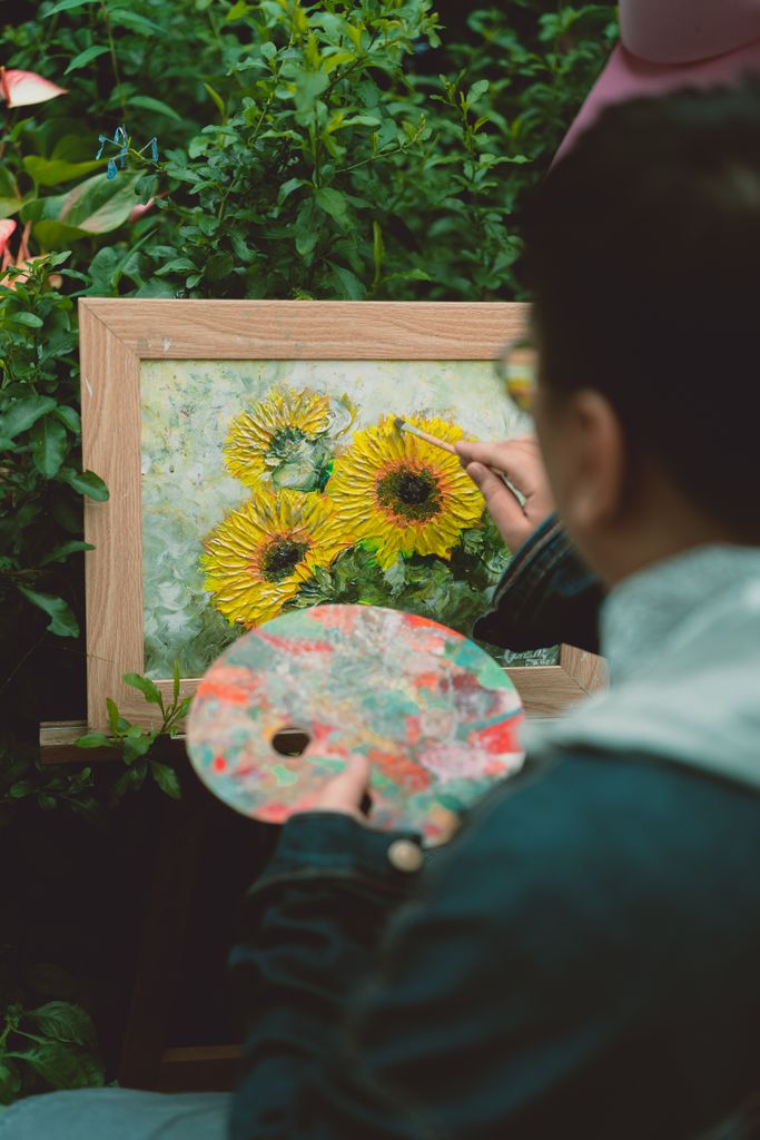Person painting vibrant sunflowers on canvas in a lush green garden. Artistic scene.